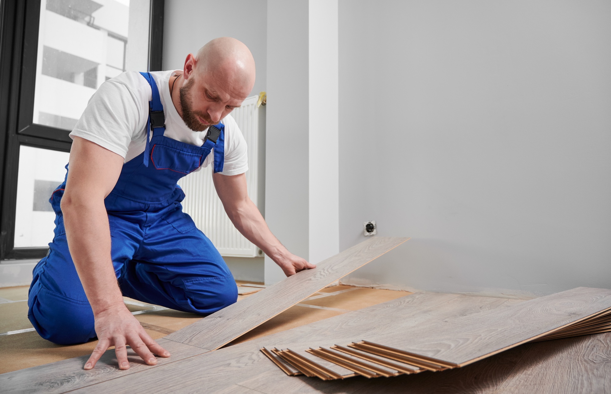 Man in workwear installing laminate flooring in apartment.